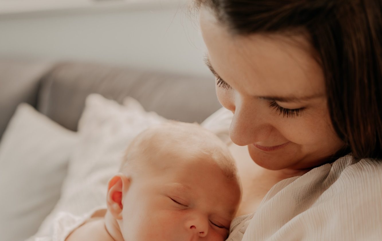 Geborgenheit und Nähe in der Babyzeit Bindungsorientierte Mutter hält ihr schlafendes Baby liebevoll im Arm
